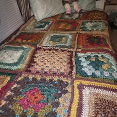 a child sitting on top of a bed covered in crocheted granny's squares