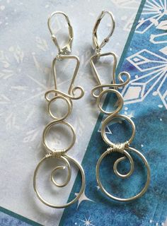 two pairs of silver earrings sitting on top of a blue and white paper with snowflakes in the background