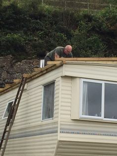 a man working on the roof of a mobile home in front of a hill side