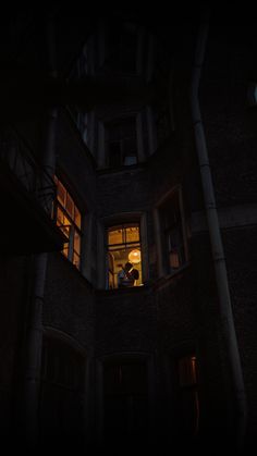 two people are standing in the window of an old building at night with their lights on