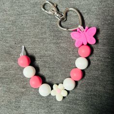 a pink and white necklace with a butterfly charm on the front is laying on a gray surface