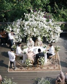 a group of people sitting around a table on top of a wooden floor covered in flowers