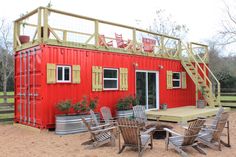 a red shipping container with lots of chairs and tables around it in front of a building