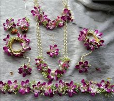 purple flowers and pearls are arranged on a white cloth with beads, rings and necklaces