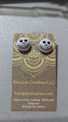 a pair of skully earrings on top of a business card for kimbien creations