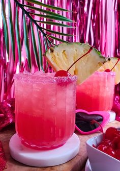 two glasses filled with pink liquid sitting on top of a table next to a pineapple