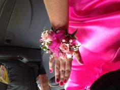 a woman in a pink dress with flowers on her wrist and hand resting on the seat