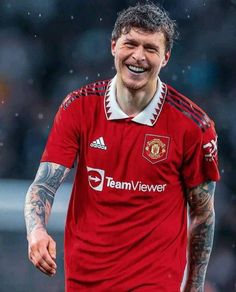 a man with tattoos on his arms and chest smiles at the camera while wearing a red shirt