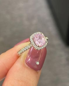 a woman's hand holding a pink diamond ring with diamonds on the band and side