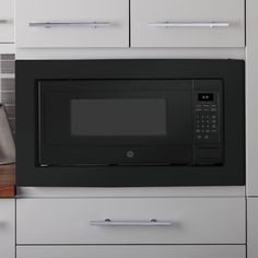 a black microwave oven sitting on top of a kitchen counter next to white cupboards