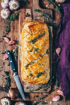 a loaf of bread sitting on top of a wooden cutting board next to garlic and herbs