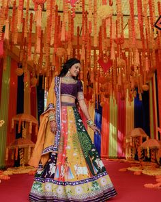 a woman in an orange and yellow lehenga standing on a stage with lots of decorations