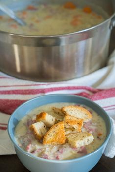 a bowl of soup with croutons in it and a silver pot behind it