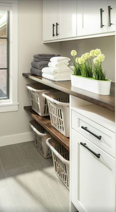 an organized laundry room with white cabinets and lots of towels on the shelves, along with baskets filled with flowers