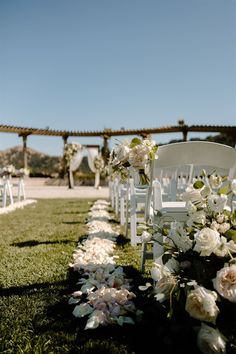 an outdoor ceremony setup with white chairs and flowers on the grass in front of it