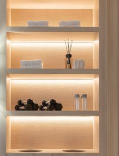 the shelves have candles, towels and other items on them in white lit space between two walls