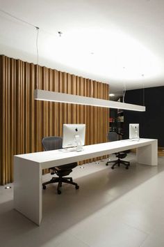 an office with two desks and chairs in front of a wall made of wooden slats