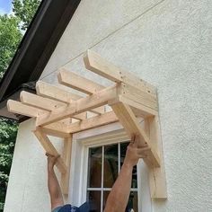 a man is working on a wooden structure in front of a window that has been built into the side of a house