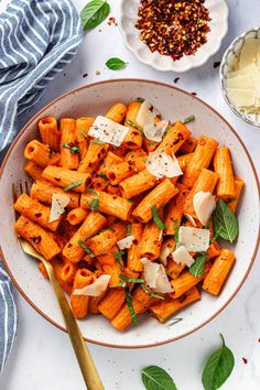 a white bowl filled with pasta and topped with parmesan cheese, basil sprinkled on top