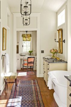 a hallway leading to a bathroom with a sink and tub in the corner, along with a rug on the floor