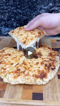 someone is cutting up a piece of cheese pizza on a wooden board with a knife