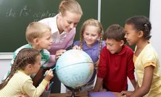 a teacher showing children how to use an earth globe in front of a chalkboard