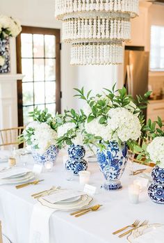 the table is set with blue and white vases, gold place settings, and candles