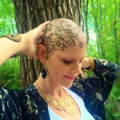 a woman with tattoos on her head stands in front of a tree and holds her hands to her hair