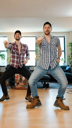 two men in jeans and plaid shirts are dancing on the floor with their hands up