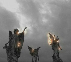 three angel statues with lights shining from their wings in front of an overcast sky