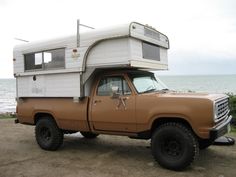 an old truck with a camper on the back parked by the water's edge