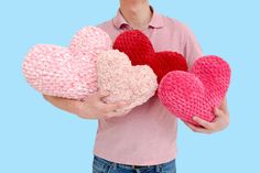 a man holding three knitted hearts in his hands on a blue and pink background