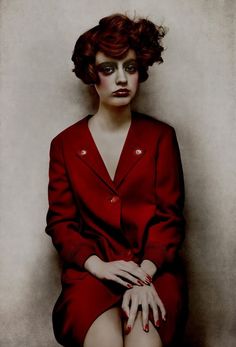 a woman in a red suit sitting on top of a white wall with her hands crossed