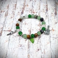 a bracelet with green and brown beads on white wooden planked floor, featuring a leaf charm