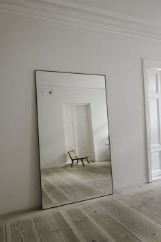 a mirror sitting on top of a wooden floor next to a white wall and door