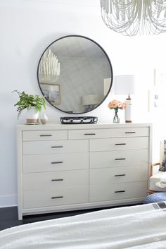 a white dresser with a round mirror above it