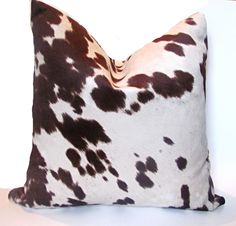 a brown and white cow print pillow sitting on top of a wooden table next to a wall