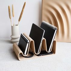 two notebooks and a pen holder on a white surface with a vase in the background