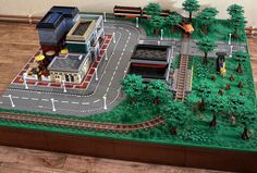 a lego model of a train station with trees and people on the tracks in front of it