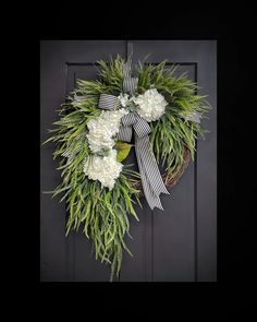 a wreath with white flowers and greenery hanging on a door