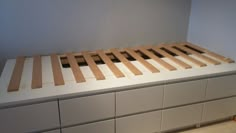 a bed made out of wooden slats on top of a white dresser in a room