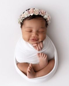 a newborn baby wearing a flower crown sleeping in a white bowl with her hands under her chin