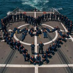 a large group of navy men standing on top of a ship in the ocean with their arms around each other