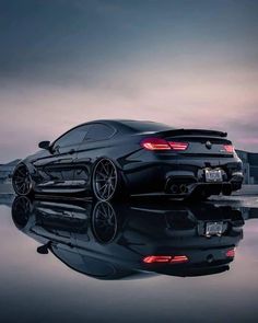 a black sports car is reflected in the water