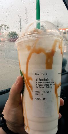 a person holding up a drink in front of a window with rain drops on it