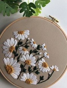 a close up of a embroidery on a table with a plant in the background and white flowers