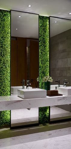 a bathroom with two sinks and green plants on the wall behind them in front of mirrors