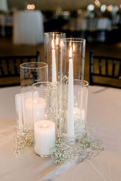 candles and flowers on a table in a room with white linens, chairs and tables