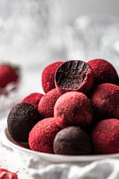 a white bowl filled with red and black chocolate truffles on top of a table