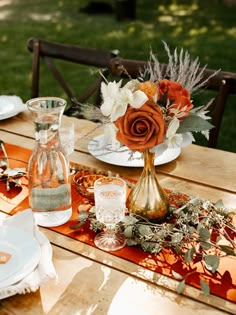 the table is set with plates, silverware and orange flowers in glass vases